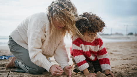 Family-building-sand-castle-on-cool-beach.-Single-mom-playing-little-curly-son