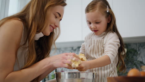 Lovely-woman-daughter-cooking-at-kitchen.-Mom-removing-pastry-from-child-hands