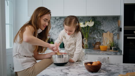 Cheerful-family-making-dough-at-home.-Girl-helping-millennial-mom-at-kitchen