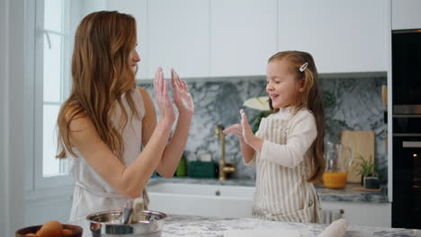 Cheerful-mom-child-clapping-hands-at-kitchen.-Playful-woman-and-girl-having-fun