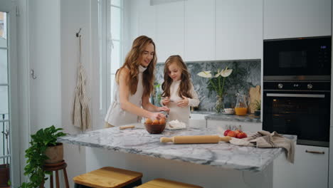 Cute-family-cooking-at-kitchen-together.-Happy-mother-daughter-sifting-flour