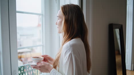 Satisfied-lady-enjoying-cup-of-coffee-at-home-closeup.-Woman-watching-window
