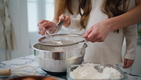 Mother-daughter-hands-sifting-flour-home-closeup.-Unknown-family-cooking-pastry