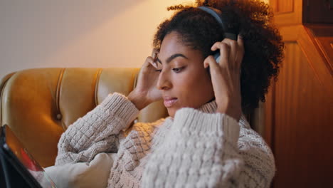 Curly-lady-wearing-headphones-comfy-home.-African-positive-woman-watching-tablet