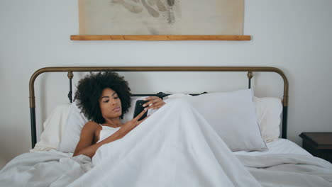 Sanftes-Modell-Liest-Smartphone-Luxusschlafzimmer.-Afrikanische-Dame-Hält-Handy