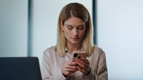 Focused-woman-texting-phone-office-portrait.-Serious-manager-at-laptop-workplace