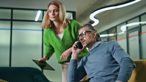 Two-colleagues-working-together-office.-Woman-consulting-with-calling-phone-man