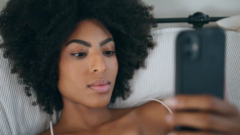 Gentle-lady-typing-smartphone-screen-bed-closeup.-Dark-skin-woman-laying-alone