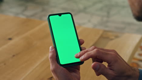 User-scrolling-chromakey-smartphone-at-cabinet-closeup.-Man-hand-holding-device