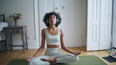 Tranquil-lady-meditating-on-carpet-zoom-out.-African-woman-sitting-lotus-pose