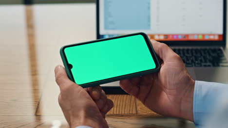 Businessman-arms-holding-mockup-smartphone-indoors.-Boss-using-green-display