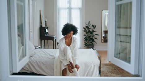 Serene-girl-wearing-socks-at-morning-bedroom.-Curly-carefree-lady-daily-routine