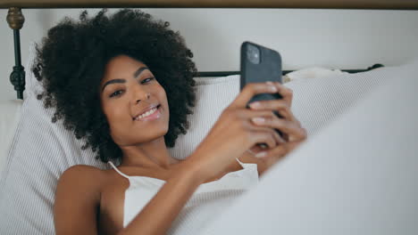 Sensual-woman-resting-cellphone-bed.-Portrait-african-curly-lady-looking-camera