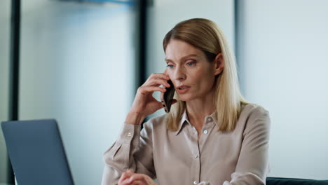 Calm-director-talking-smartphone-at-office-close-up.-Serious-lady-making-call