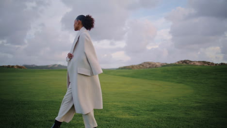 African-american-walking-green-grass-field-on-cloudy-day.-Serene-model-admiring