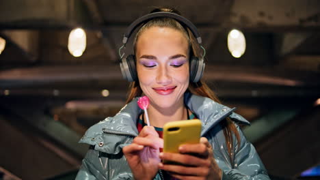 Woman-listening-music-walking-at-night-closeup.-Girl-headphones-holding-lollipop