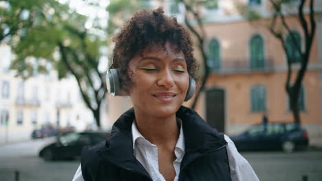 Una-Mujer-Africana-Disfruta-De-Una-Canción-Con-Auriculares-Inalámbricos-En-La-Calle-De-Cerca-Verticalmente
