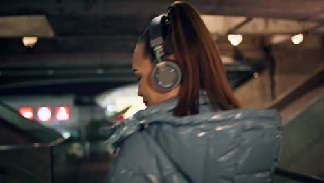 Woman-walking-dark-subway-in-headphones-listening-music-close-up-back-view
