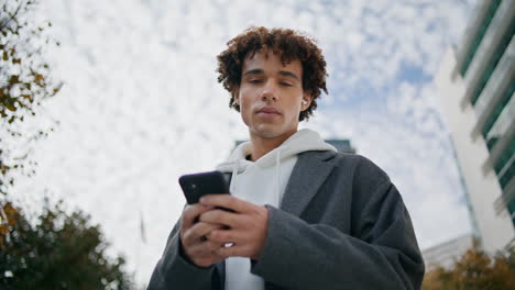 Young-man-using-phone-outdoors-portrait.-Earphones-teenager-listening-music