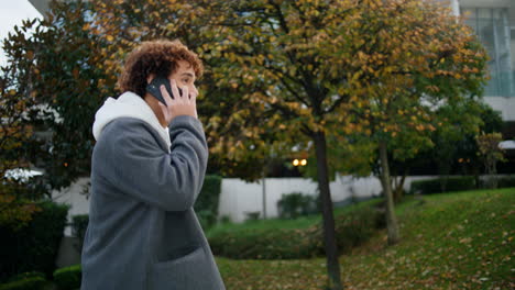 Curly-teen-calling-phone-street-closeup.-Young-man-walking-stairs-in-autumn-park