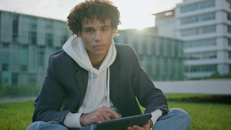 Young-man-holding-tablet-at-grass-portrait.-Curly-youngster-looking-camera