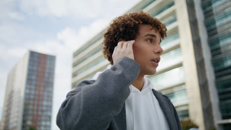 Focused-teenager-talking-earphones-street-portrait.-Curly-guy-touching-earbuds