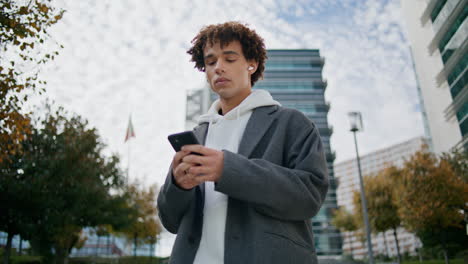 Earphones-guy-listening-music-at-downtown-zoom-on.-Young-man-holding-smartphone