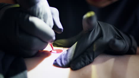 Artist-hands-tattooing-red-ink-on-skin-closeup.-Master-working-machine-at-studio