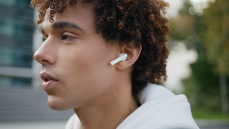 Serious-model-face-talking-earphones-at-street-portrait.-Curly-guy-using-earbuds