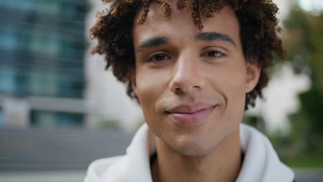Curly-guy-face-posing-city-portrait.-Young-man-looking-camera-smiling-on-street