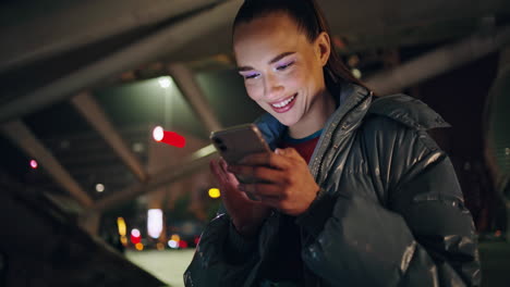 Cheerful-girl-scrolling-social-network-standing-at-night-city-street-close-up.