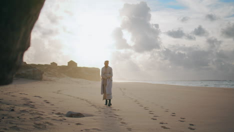 Peaceful-model-walking-sand-beach-leaving-footprints.-Travel-woman-turning-back