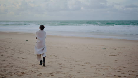 Lonely-woman-walking-beach-on-cloudy-day.-Calm-tourist-watching-ocean-waves-rear