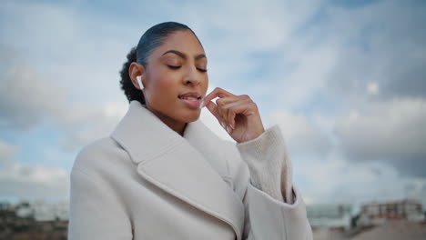 Beautiful-woman-talking-earbuds-on-go-closeup.-Relaxed-african-american-walking