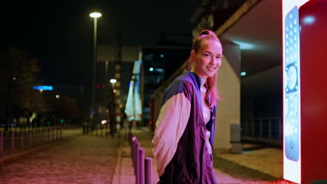 Girl-standing-night-lights-looking-camera-with-smile.-Woman-enjoy-evening-time.