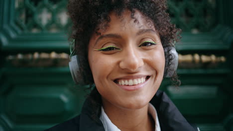 Portrait-smiling-girl-headphones-standing-near-vintage-door.-Woman-in-earphones