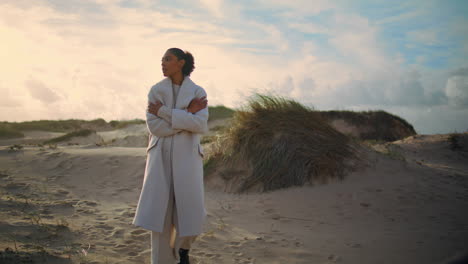 Lonely-woman-admiring-beach-dunes.-Black-hair-model-get-cold-resting-seaside