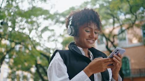 Cheerful-lady-listening-music-by-headphones-holding-phone-close-up-vertical