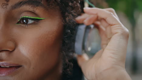 Closeup-woman-face-headphones-looking-camera-outdoors.-African-girl-in-earphones
