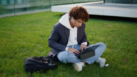 Estudiante-Serio-Escribiendo-Una-Computadora-Portátil-En-El-Parque-Urbano.-Joven-Relajado-Sentado-En-La-Hierba
