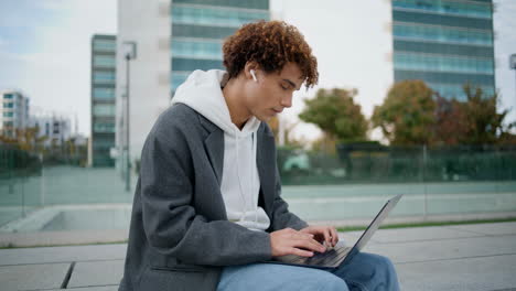 Young-freelancer-working-computer-at-street-closeup.-Curly-guy-chatting-laptop