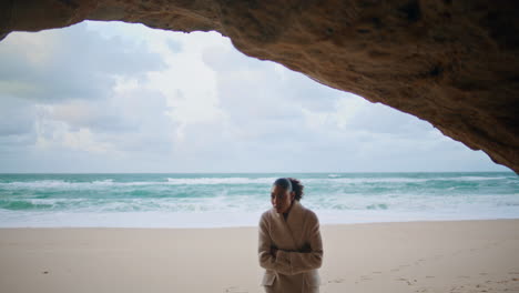 Peaceful-traveler-explore-seashore-walking-beach.-Curly-woman-hiding-ocean-cave