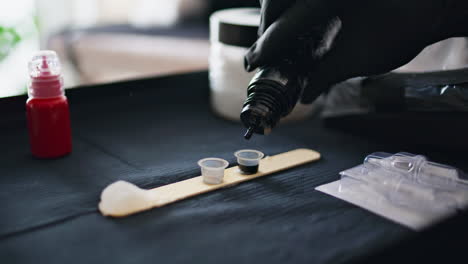 Tattooist-hand-dropping-ink-at-workplace-closeup.-Master-pouring-black-colour