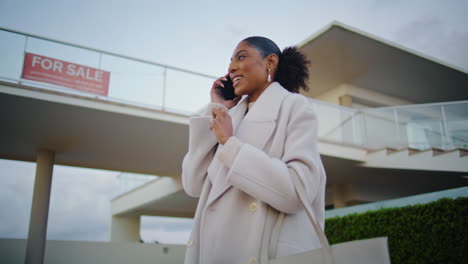 Realtor-talking-phone-client-at-house-for-sale.-Happy-african-american-discuss
