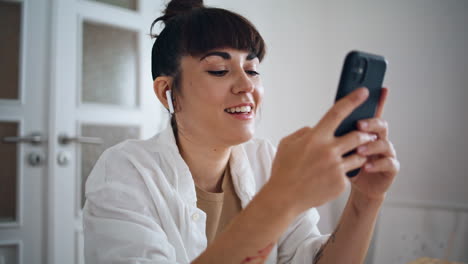 Smiling-artist-holding-smartphone-home-close-up.-Earphones-woman-listening-music