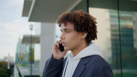 Young-man-having-mobile-call-at-glass-balcony-close-up.-Curly-guy-using-phone