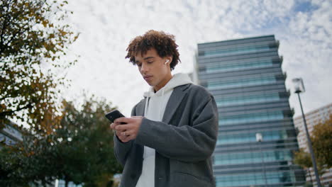 Curly-teenager-typing-smartphone-at-street-closeup.-Young-man-listening-music