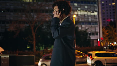 Curly-ceo-talking-telephone-in-dark-street.-Business-traveler-pulling-suitcase
