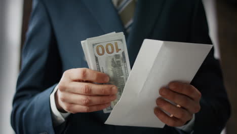 Man-taking-money-envelope-indoors-close-up.-Hands-holding-american-dollars.