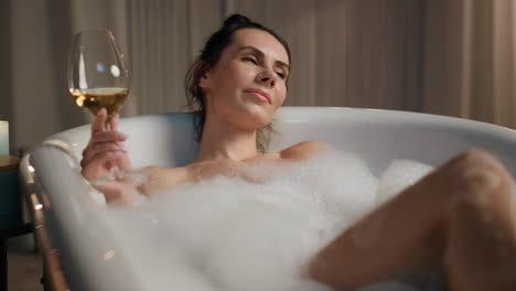 Charming-lady-holding-wine-glass-laying-bubble-bath.-Spa-girl-enjoying-alcohol